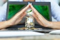 Protection of money from online transaction concept, with womanÃ¢â¬â¢s hands covering a jar of coins above a notebook Royalty Free Stock Photo